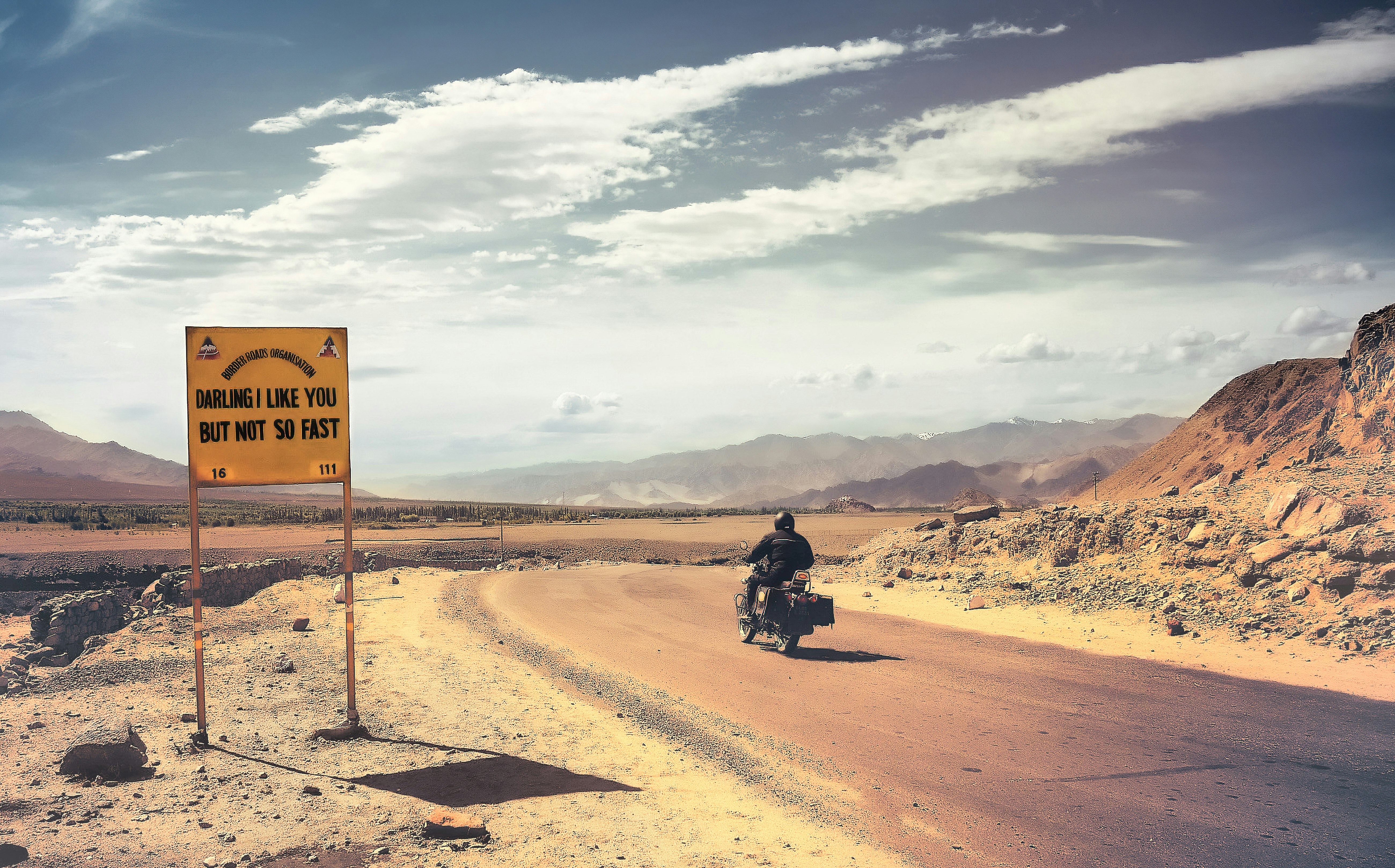 man in black motorcycle on brown sand under white clouds and blue sky during daytime